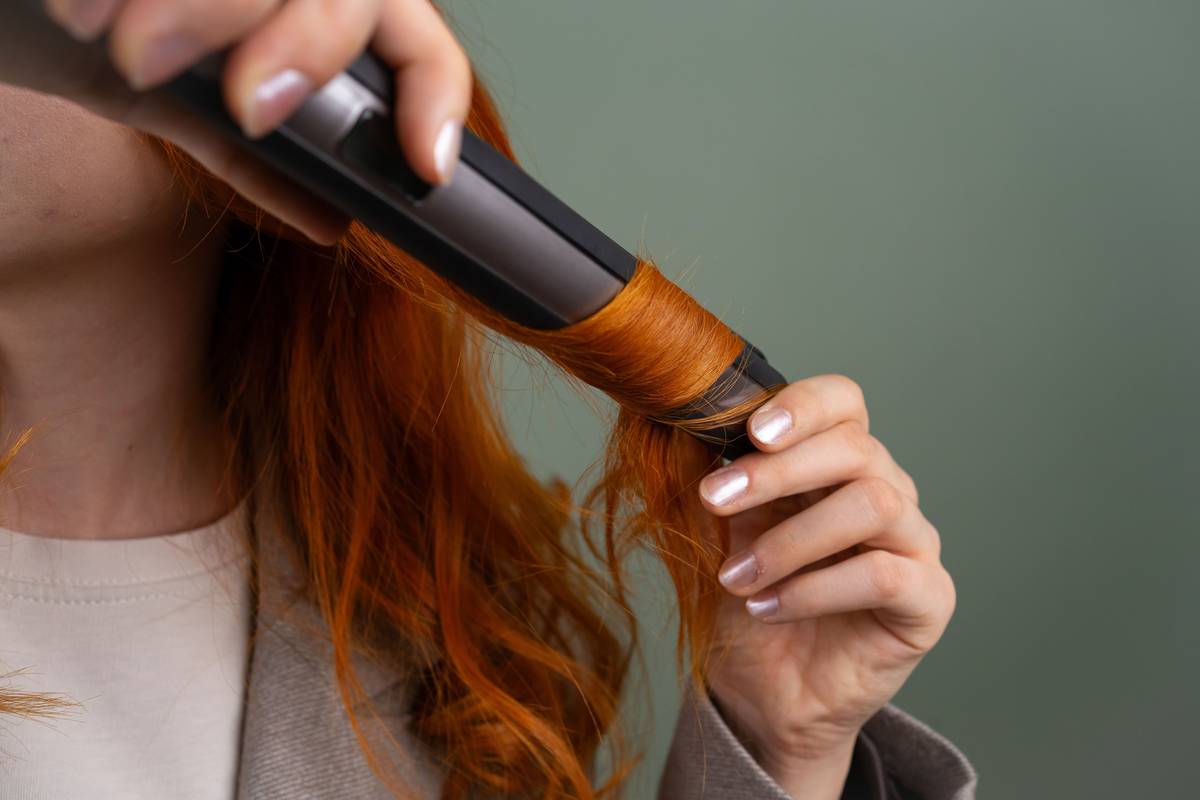 Woman using a curling brush to style shoulder-length hair, creating soft waves with a heated rotating barrel
