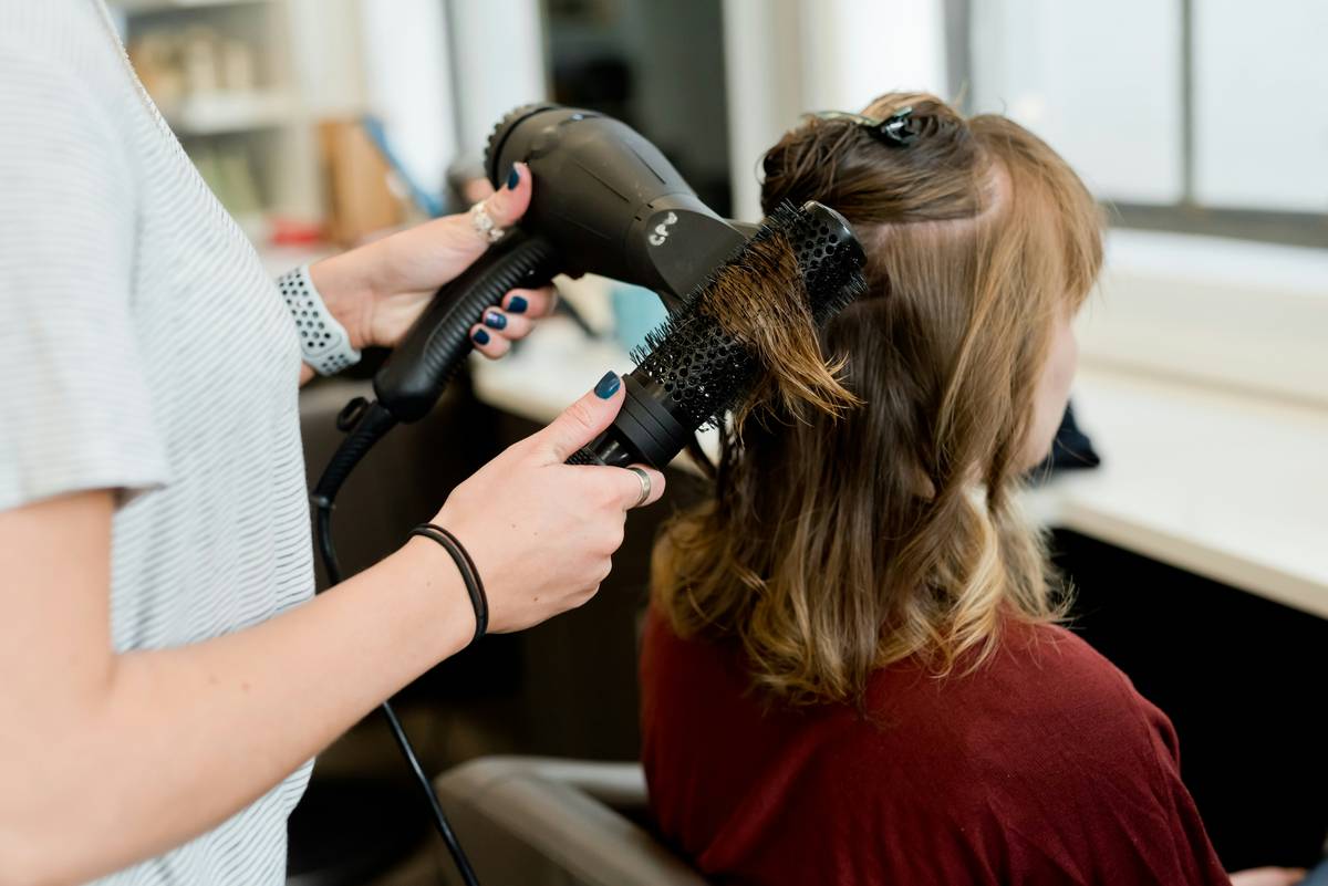 Close-up of a professional hair styling iron gliding through thick, wavy hair with steam rising from smooth plates